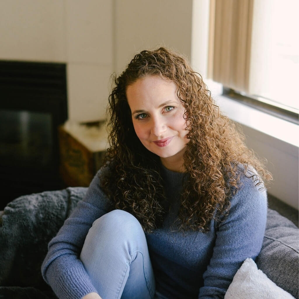 Emily Lycopolus Headshot Sitting on a grey couch